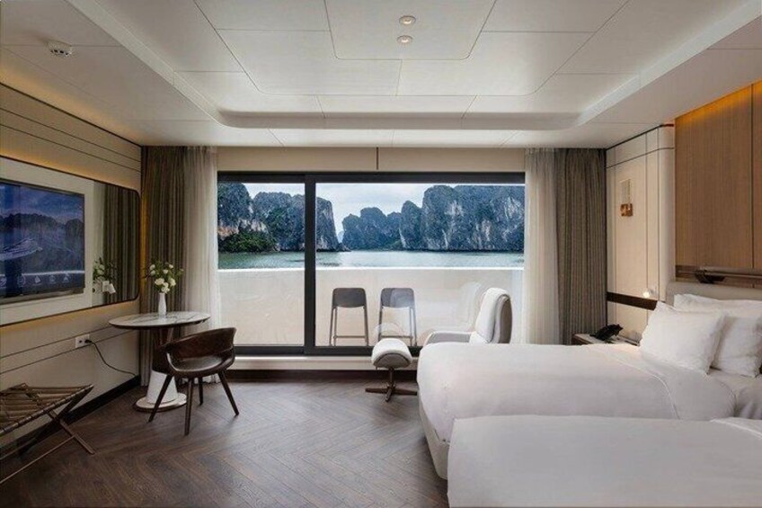 A hotel room with a bed, a desk, two chairs, and a large window overlooking a body of water. 3
