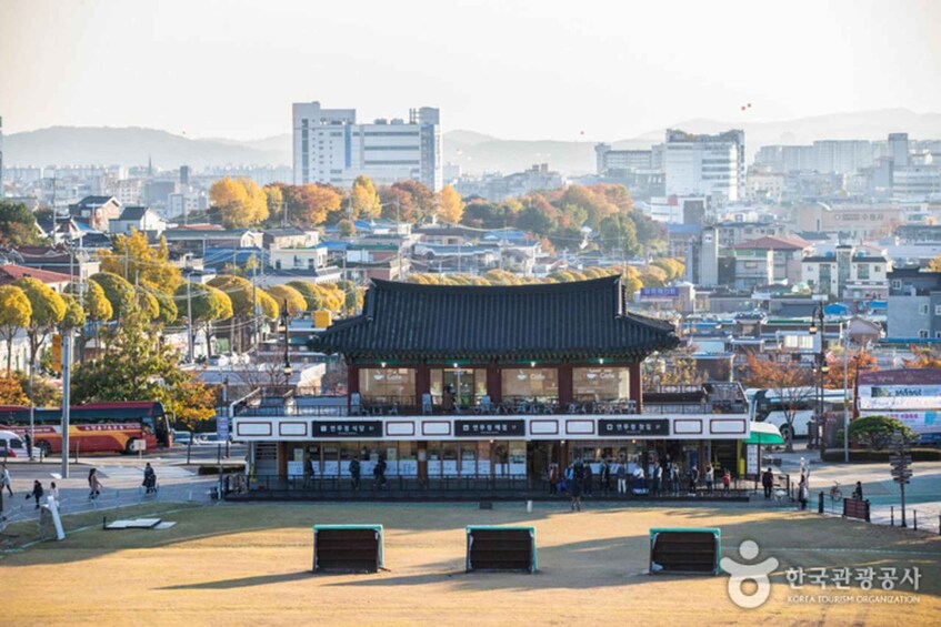 A traditional Korean building with a tiled roof, surrounded by a park with benches and a road with vehicles. 3