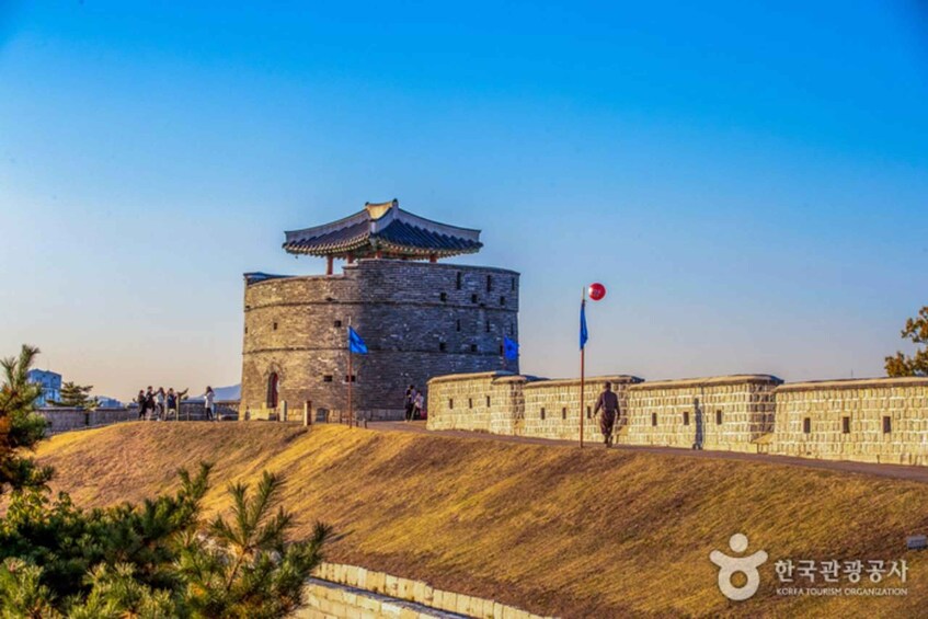 A historic stone tower with a traditional roof, surrounded by a stone wall and a flagpole with a red flag. 4