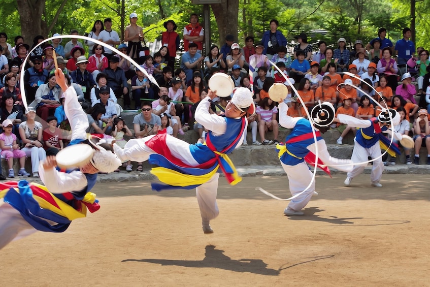 A group performing a traditional dance with fans, surrounded by an audience. 1