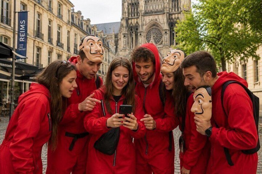 Un grupo de personas con chaquetas rojas reunidas alrededor de un teléfono inteligente, con un edificio histórico al fondo. 1