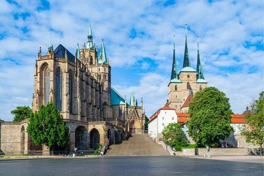 A historic cathedral with multiple spires, a large archway, and a tree-lined street. 2