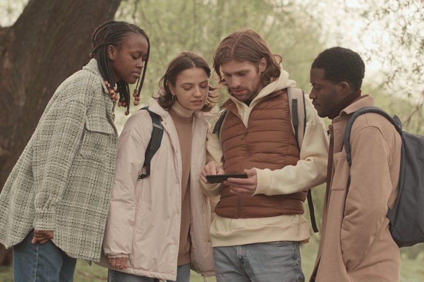 Four people standing outdoors, one holding a smartphone. 2