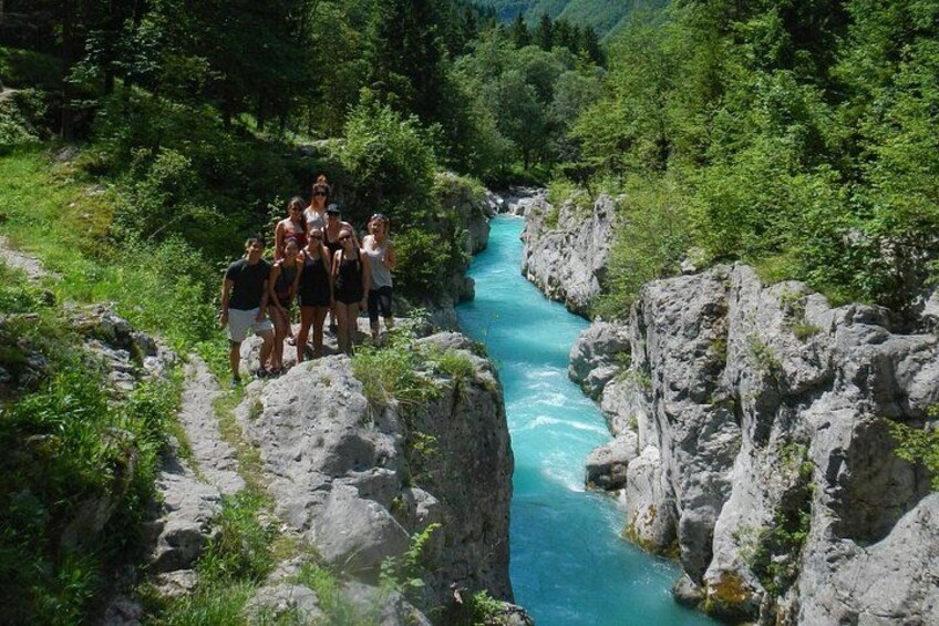 A group of people standing on a rocky ledge overlooking a turquoise river surrounded by lush greenery. 3