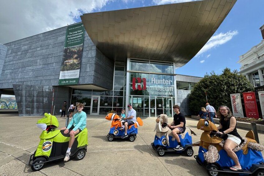 Menschen fahren mit kleinen, bunten Fahrzeugen vor dem Hunter Museum of American Art. 1