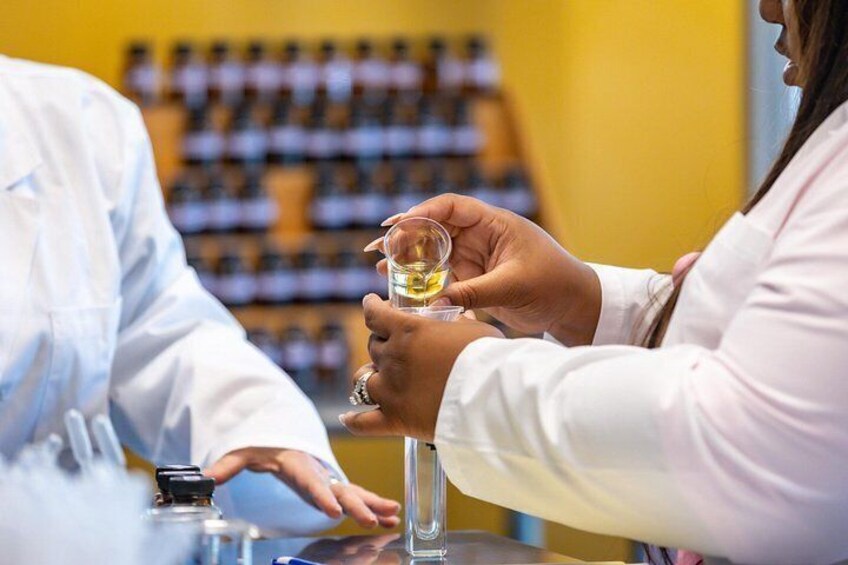 Una persona sosteniendo un vaso con líquido, posiblemente una bebida, en un laboratorio con estantes llenos de botellas al fondo. 1