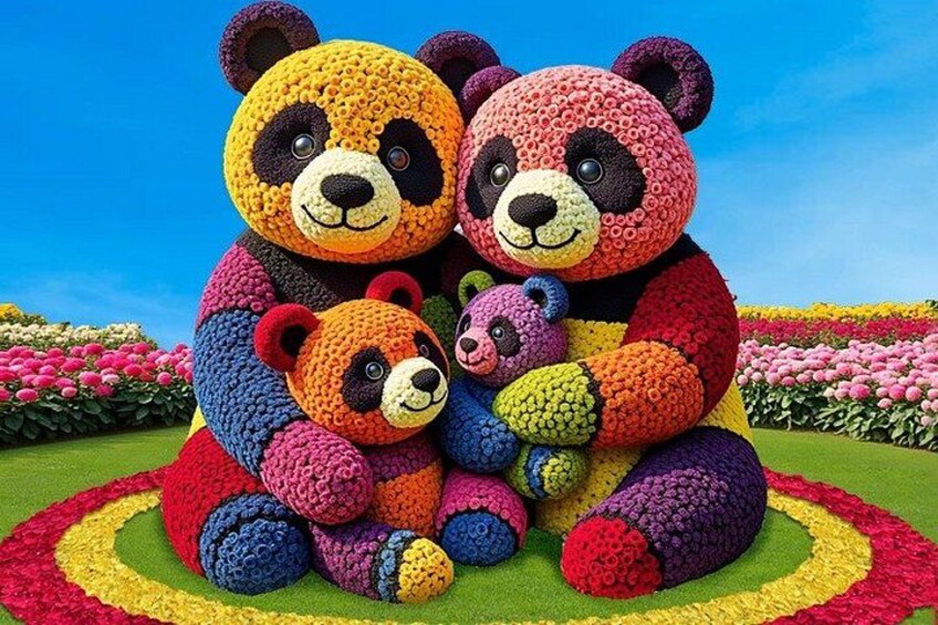 A large, colorful teddy bear sculpture surrounded by a circular flower bed. 5