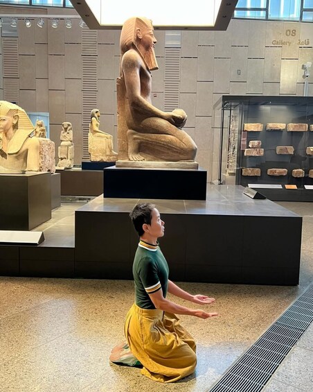 Une personne à genoux dans un musée, avec des statues de l’Égypte ancienne en arrière-plan. 1