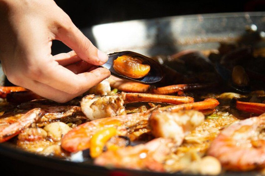 A hand holding a clam, seafood, and vegetables on a grill. 5