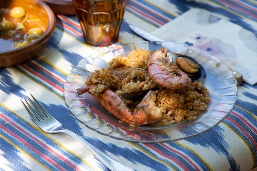 A plate of rice with shrimp and mussels, a glass of drink, and a fork on a striped tablecloth. 2