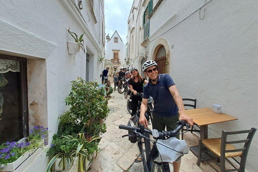 Une rue étroite où sont garés des vélos le long des trottoirs, une table et des chaises disposées pour prendre les repas en plein air, et des bâtiments aux façades blanches et aux fenêtres en arc de cercle. 4