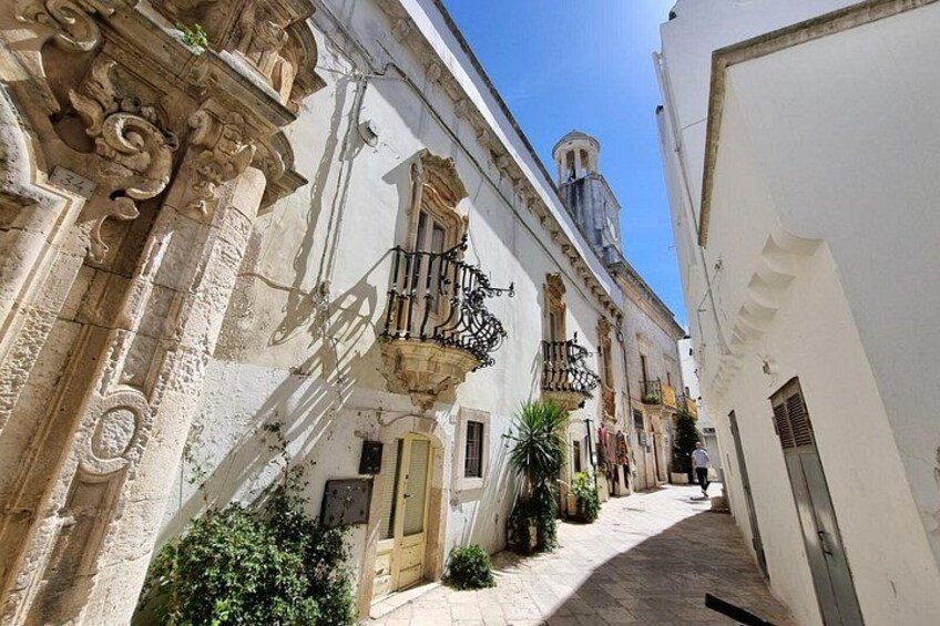 A narrow street with ornate buildings, a bell tower, and a clear blue sky. 3