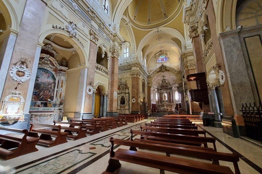 An ornate church interior with rows of wooden pews and detailed frescoes on the walls. 2