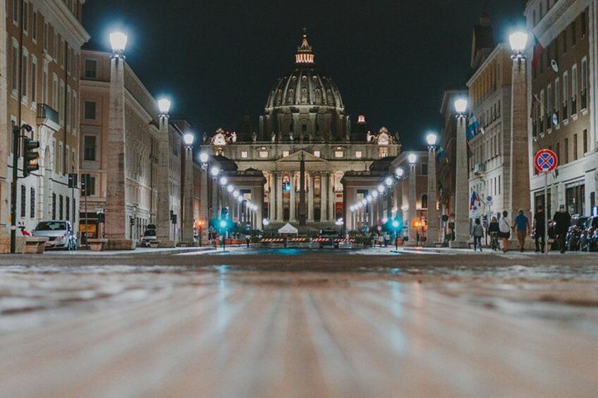 A nighttime view of a grand, illuminated building with a dome, flanked by street lamps and buildings. 3