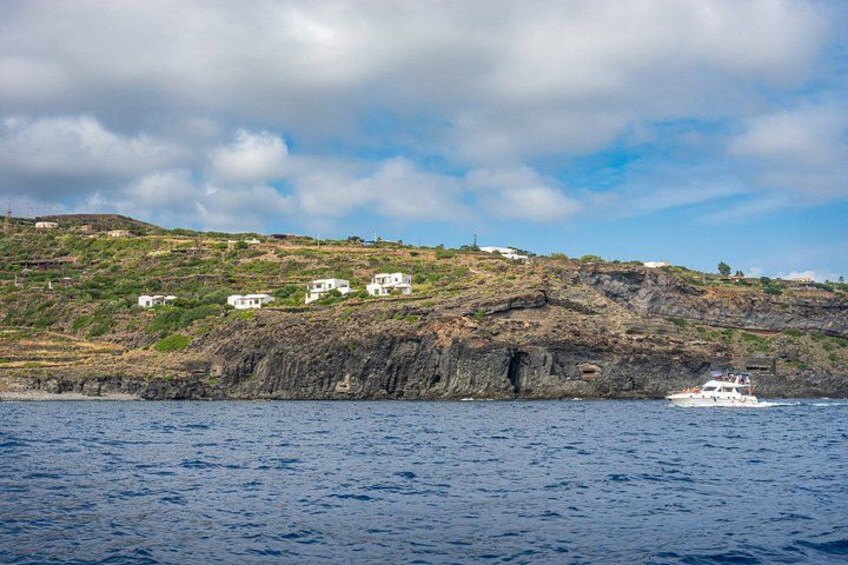 A coastal landscape with white buildings on a hillside, a rocky cliff, and a boat on the water. 3