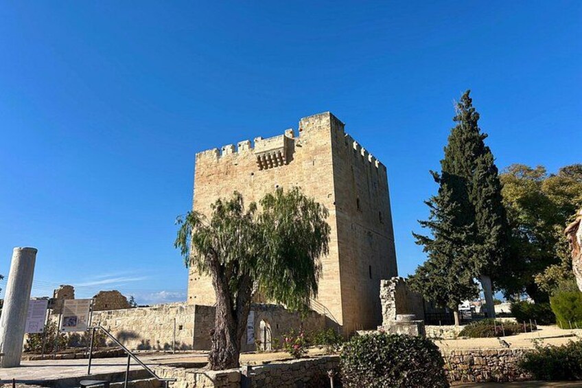 A historic stone tower with a square base and crenellated top, surrounded by trees and ruins. 3