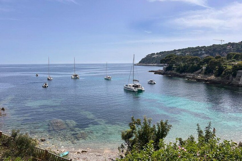 Paesaggio costiero con acqua turchese cristallina, vele bianche e una costa rocciosa con vegetazione. 4