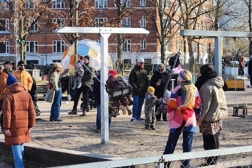 Un parque público con gente, un área de juegos y edificios al fondo. 3