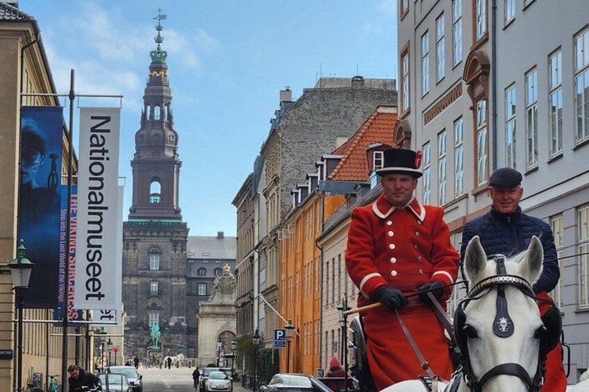 A historical reenactment with a person in a red uniform on horseback, a horse, and a tall church tower in the background. 5