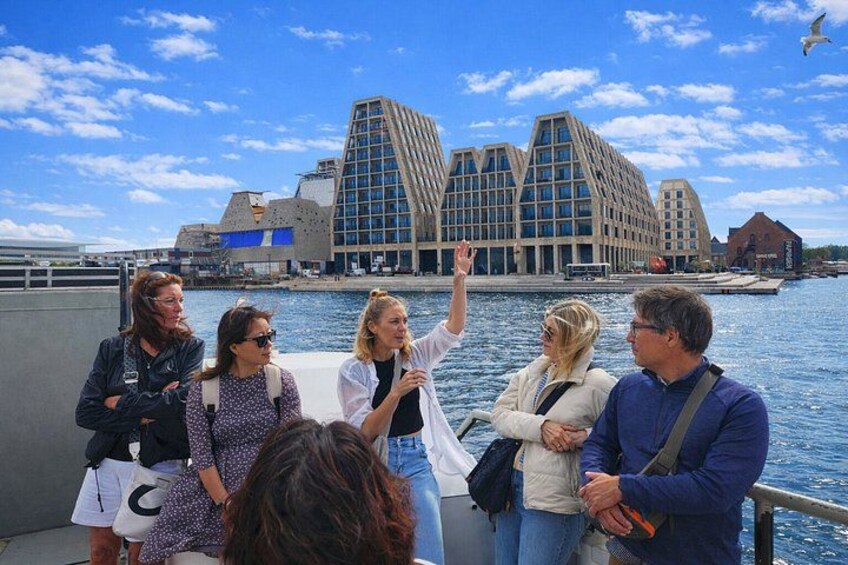 Een groep mensen op een boot, met een modern gebouw op de achtergrond. 2