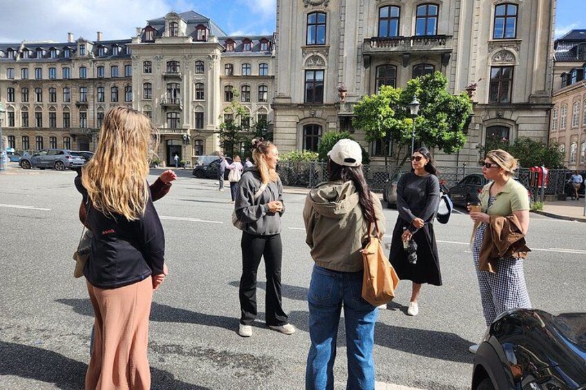 Eine Gruppe von Menschen steht auf einer Straße mit historischen Gebäuden im Hintergrund. 4