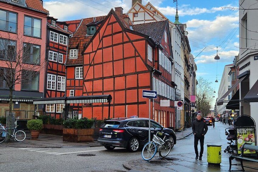 Eine Straße mit traditionellen Fachwerkhäusern, einem abgestellten Fahrrad, einem Auto und einer Person, die gerade geht. 5