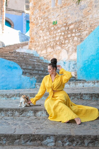 A person in a yellow dress sitting on stone steps with a cat. 2