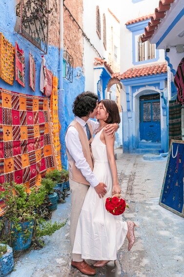 A couple embracing in a narrow street with colorful textiles and blue buildings. 5