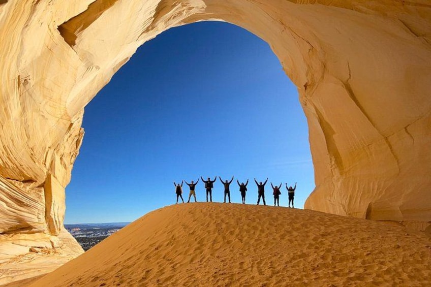 Un grupo de personas de pie bajo una formación natural de arco de roca, con un cielo azul despejado. 1