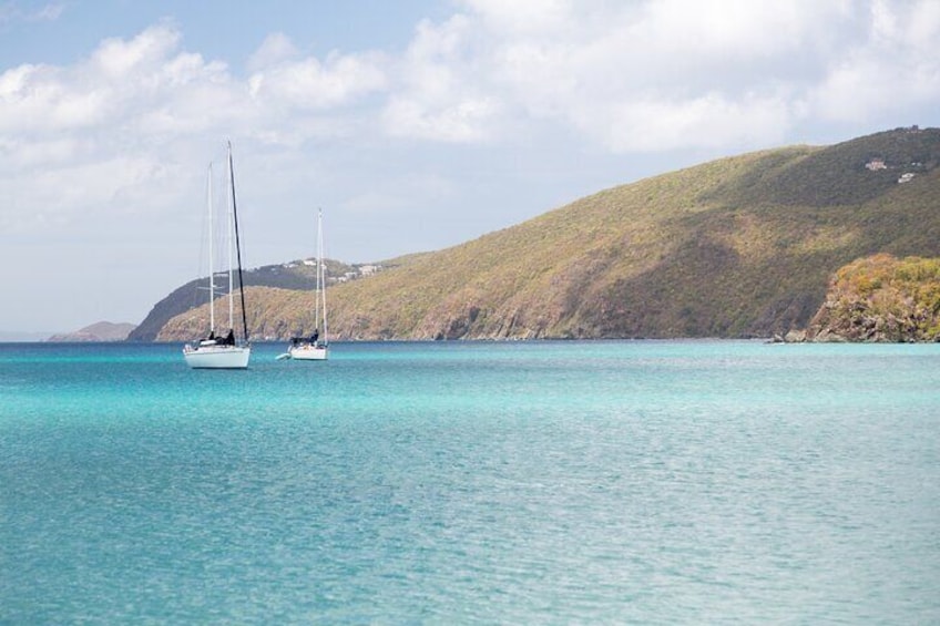 Two sailboats on turquoise water with a hilly landscape in the background. 2