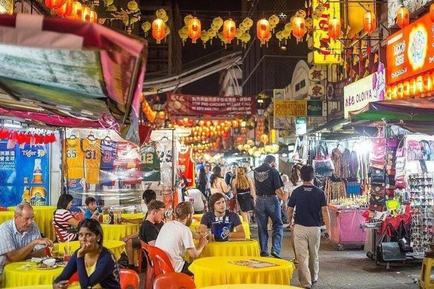 A bustling street market with yellow tables, people walking, and various shops. 2