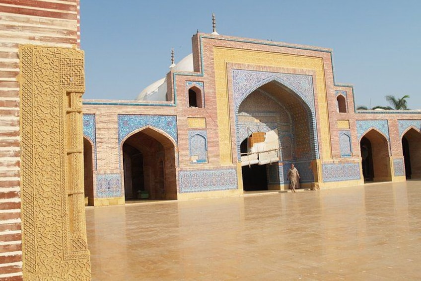 Un grand bâtiment imposant, richement décoré, avec une arche centrale, entouré d’une cour dallée. 2