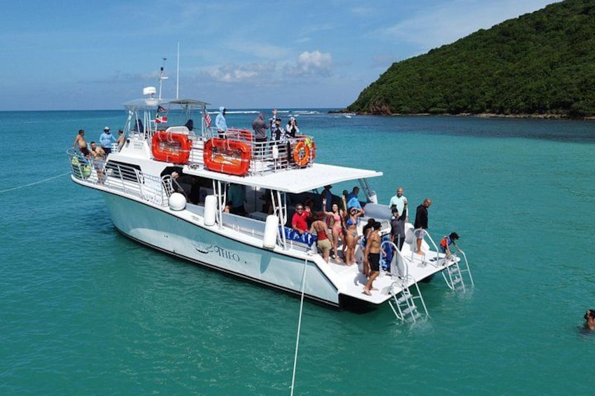 A boat with people on board, surrounded by clear turquoise water and a green island in the background. 1