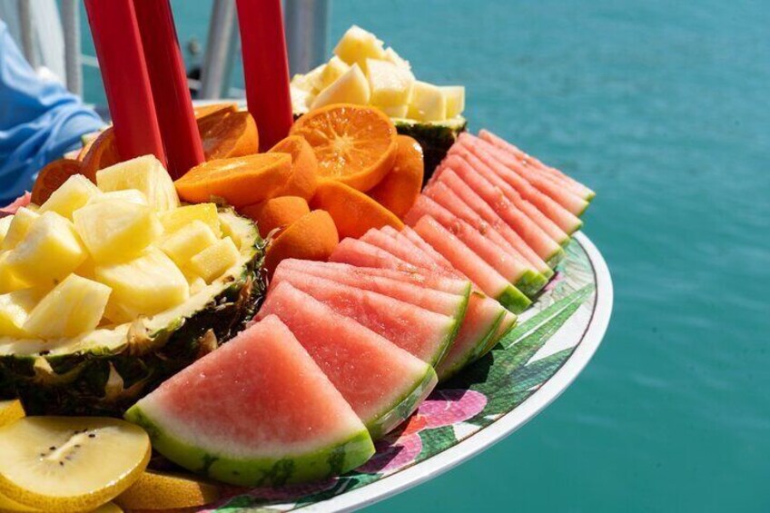 Una bandeja de frutas con sandía, piña, rodajas de naranja y limón sobre un bote. 2