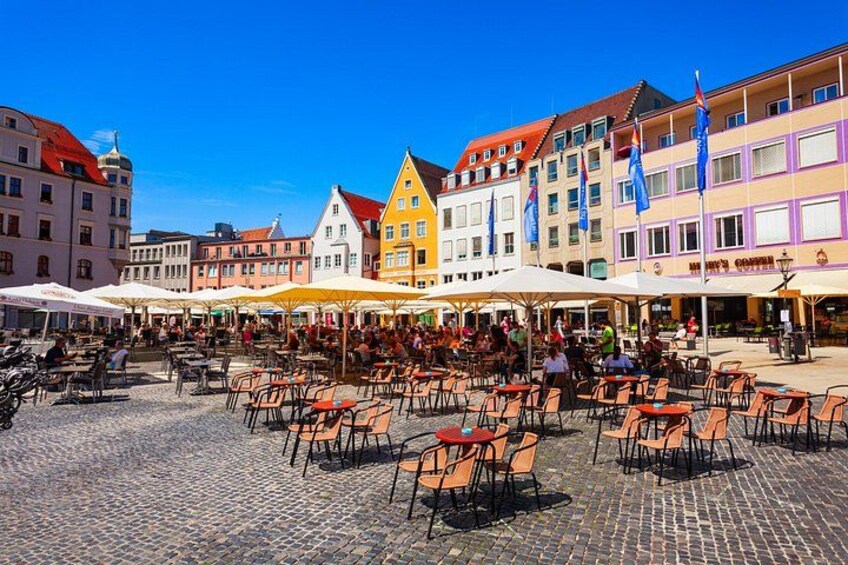 A cobblestone square with outdoor seating and colorful buildings. 1