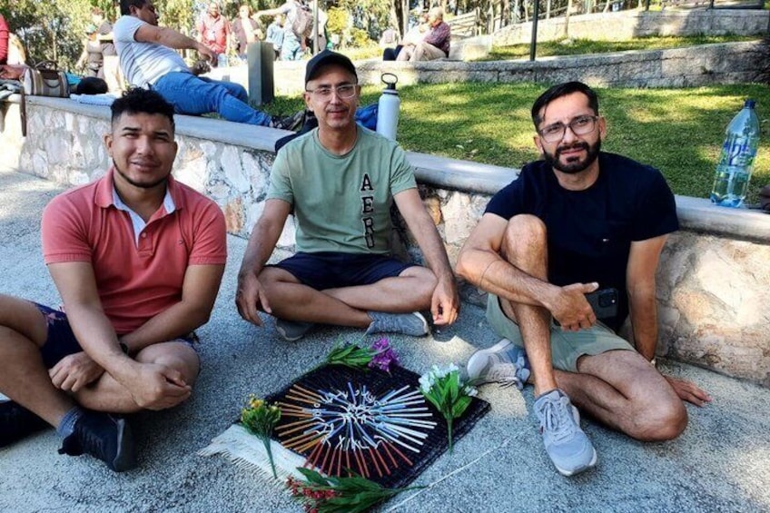 Three people sitting on a stone bench in a park with a decorative flower arrangement in front of them. 5