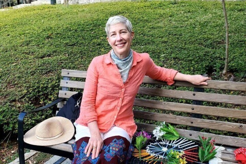 A person sitting on a wooden bench with a hat and a floral arrangement beside them. 4