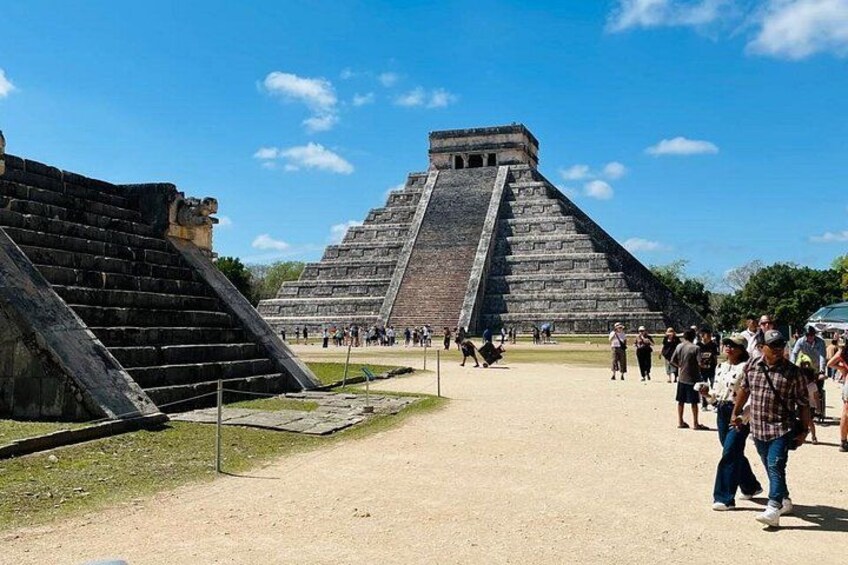 En stor pyramideformet struktur med en trappe, omgivet af et sandområde hvor folk går rundt. 2