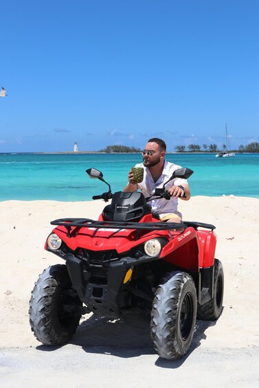 A red ATV on a sandy beach with a clear blue sky and a lighthouse in the background. 3