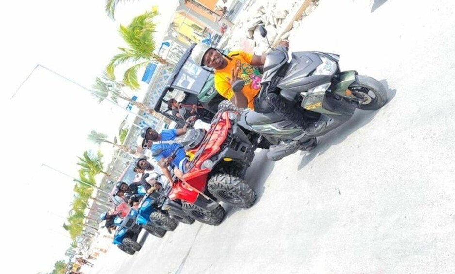 A group of people on ATVs on a street with palm trees and buildings in the background. 2