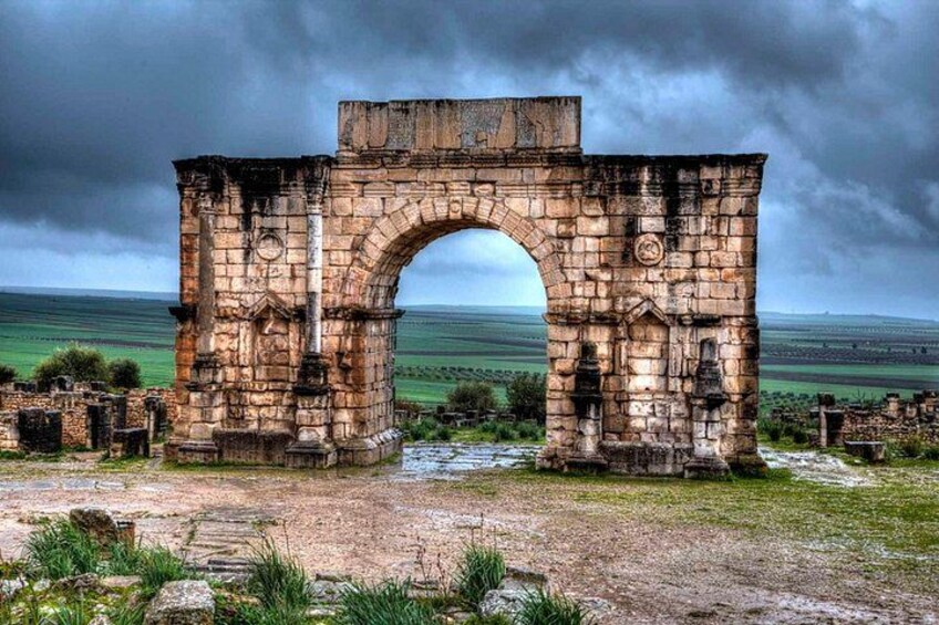 An ancient stone archway with intricate carvings, set against a backdrop of a cloudy sky and a vast, open landscape. 3