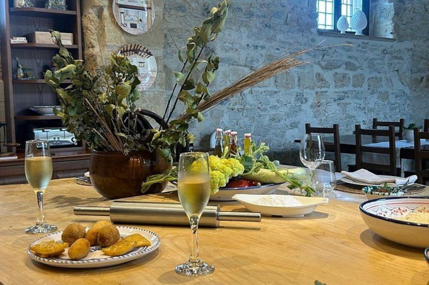 A rustic dining table with a vase of greenery, a bowl of bread, and wine glasses. 2