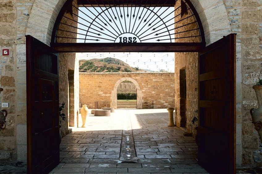 An arched entrance with a metal sign reading '1852' and a paved pathway leading to a brick building. 1