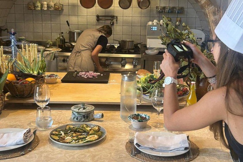 A kitchen with a chef preparing food, a dining table set with plates, glasses, and a basket of vegetables. 4