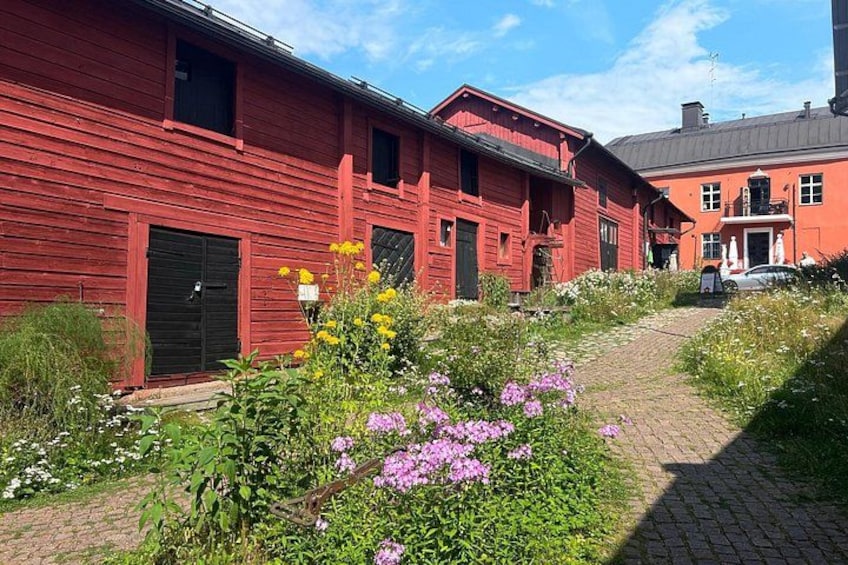A red wooden building with a brick pathway and flowering plants. 2