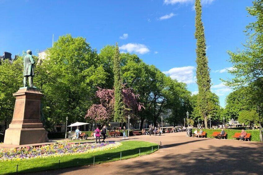 A park with a statue, tall trees, and a flower bed. 2