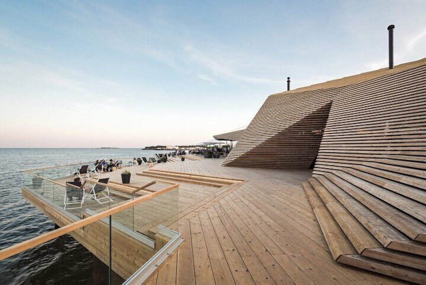 A wooden deck extending over water with chairs and a glass railing. 4