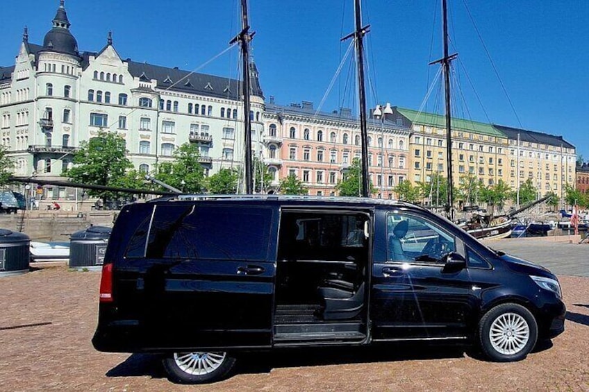 A black van parked on a dirt surface with a historic building in the background. 1
