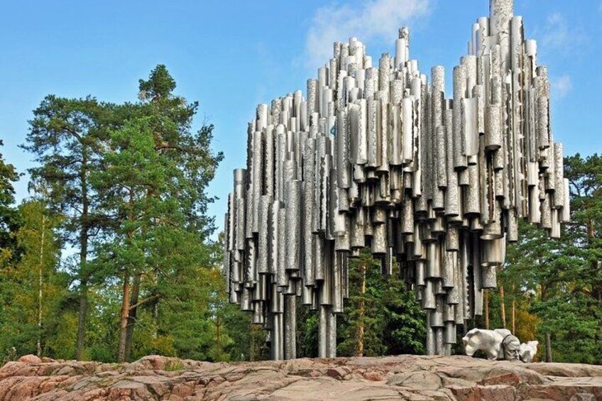 Una gran escultura abstracta hecha de elementos verticales y cilíndricos, en un entorno natural con árboles y rocas. 2