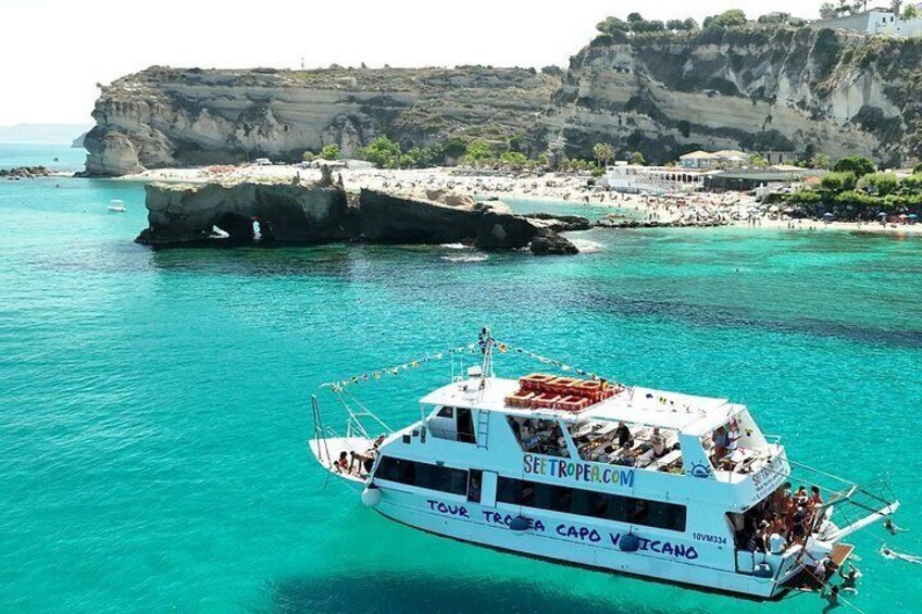 A boat named 'TURCA CAPO VATICANO' on turquoise waters with a rocky coastline and buildings in the background. 3